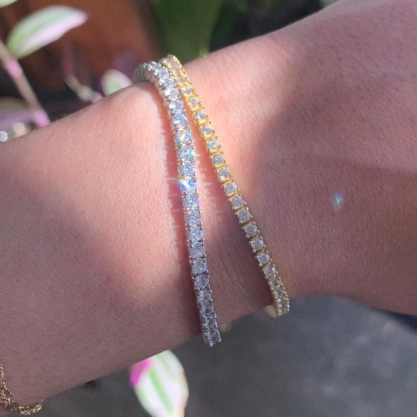View of 2 crystal tennis bracelets in sterling silver and 14k gold over silver in partial sunlight on ladies wrist.