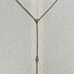 Close up of a lariat style necklace with 9 petite round cut, bezel set diamonds cast in 14 kt yellow gold settings on a body form for perspective.