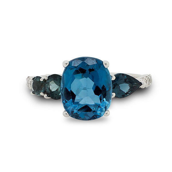 Front view of cushion cut, London blue topaz with 2 round and 1 pear cut green tourmaline stones, and 8 round cut diamonds going down the band cast in 14 kt white gold.  
