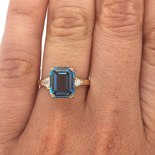 
                  
                    Load image into Gallery viewer, Emerald cut London blue topaz and round and trillion cut diamond ring cast in 14 kt yellow gold on left ring finger.
                  
                