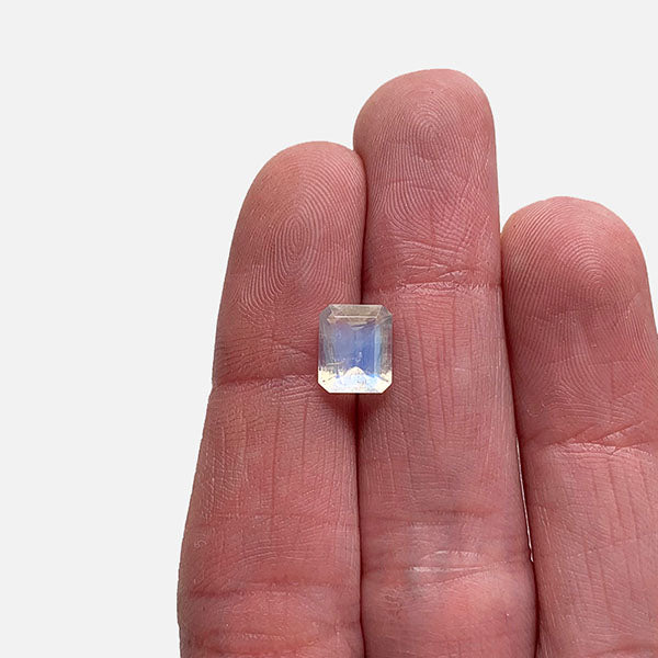 Front view of a 1.60 ct. emerald cut moonstone displaying a blue flash across face of stone. Placed in ladies hand for scale.