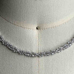 Close up of a necklace with round cut crystals set in a 925 sterling silver cluster setting on a body form for scale.