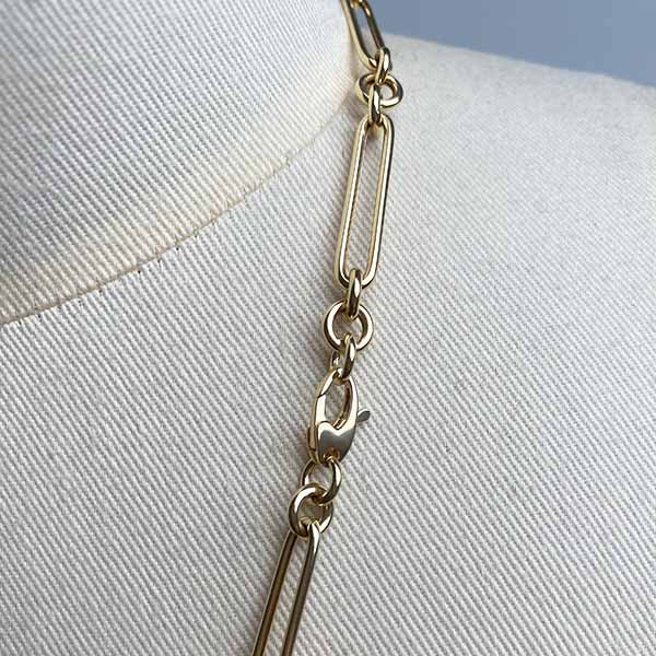 Close up image of oval clasp on larger paperclip chain with 3 round link in 14kt yellow gold.