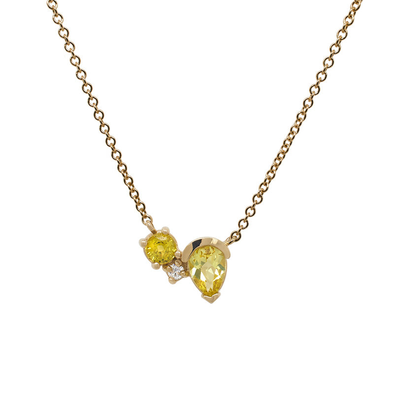 Front view of an asymmetrical round and pear cut yellow sapphire and round cut diamond necklace cast in 14 kt yellow gol