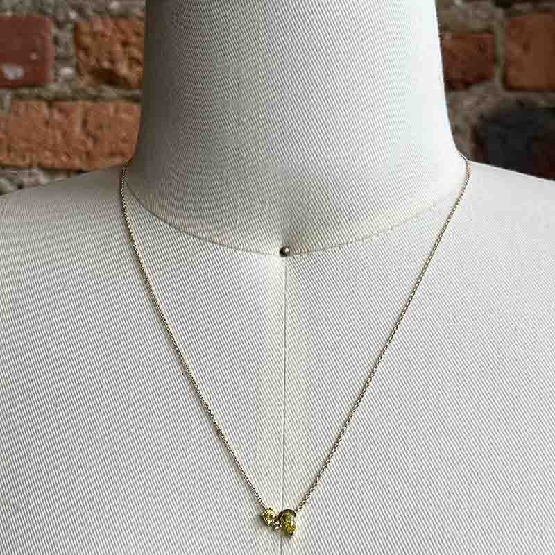 Front view of an asymmetrical round and pear cut yellow sapphire and round cut diamond necklace cast in 14 kt yellow gold. Shown on a body form for scale.