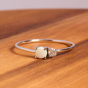 
                  
                    Load image into Gallery viewer, Front view on wood of a cabochon opal and round diamond ring on a dainty band cast in 14 kt white gold.
                  
                