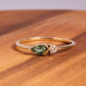 
                  
                    Load image into Gallery viewer, Front view on wood of pear cut, green tourmaline and diamond ring cast in 14 kt yellow gold.
                  
                