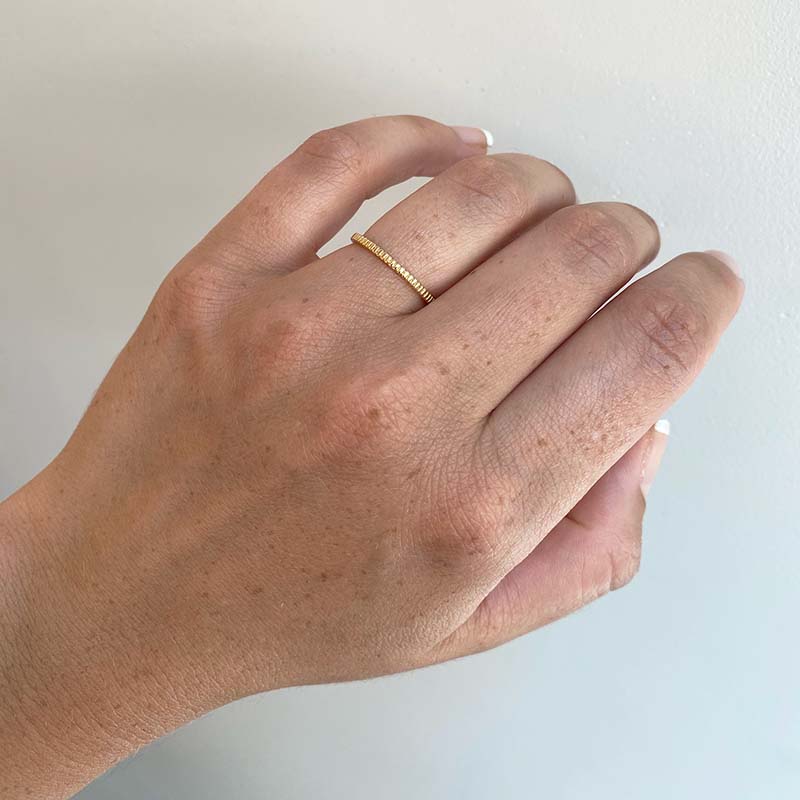 Front view on left ring finger of ring with a lined pattern cast in 18 kt yellow gold.