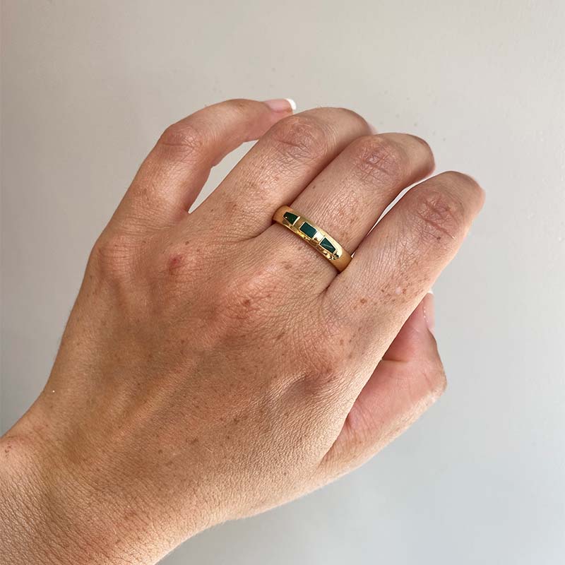 Front view on left middle finger of 4.6mm wide and rounded band with 3 inlays of malachite, rectangular in shape in the middle and tapered on either side. Cast in 14kt yellow gold.