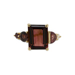 Front view of an asymmetrical, emerald cut deep red tourmaline ring with a half moon cut and round cut pink sapphires and diamonds cast in 14 kt yellow gold.