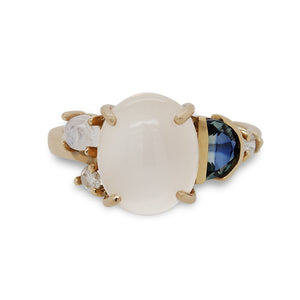 
                  
                    Load image into Gallery viewer, Asymmetrical ring with a large cabochon moonstone flanked by a smaller moonstone, diamond and half moon cut blue topaz and cast in 14 kt yellow gold.
                  
                