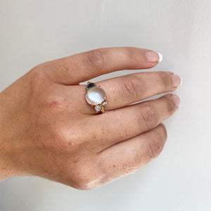 
                  
                    Load image into Gallery viewer, Front view on left ring finger of an asymmetrical ring with a large cabochon moonstone flanked by a smaller moonstone, diamond and half moon cut blue topaz and cast in 14 kt yellow gold.
                  
                