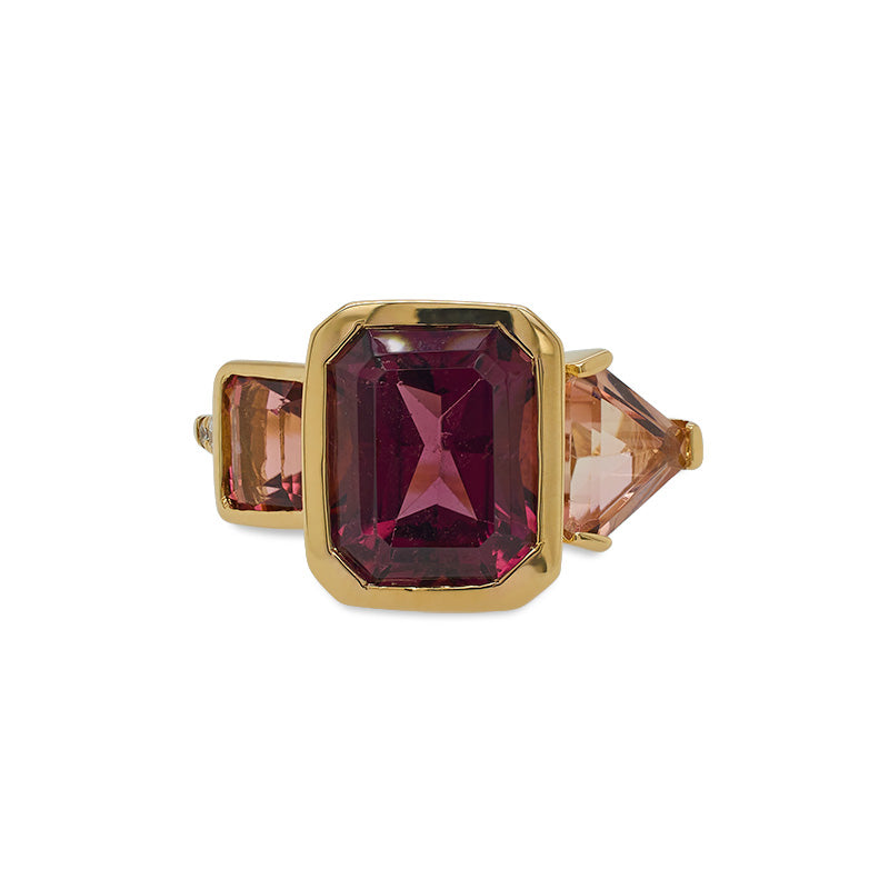 This front view of a ring is cast in 18 kt yellow gold has a large 3.5 carat emerald cut rhodolite garnet in the center and is flanked by almost 2 carats of peach colored emerald and trillion cut tourmalines and tiny round cut diamonds.