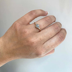 
                  
                    Load image into Gallery viewer, Front view on left ring finger of a round cut salt and pepper diamond ring flanked by 2 baguette cut diamonds, and cast in 14 kt yellow gold.
                  
                