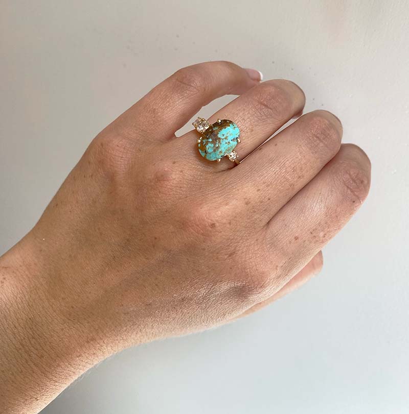 Front view on left ring finger of an asymmetrical rose cut turquoise ring flanked by 3 rose cut diamonds cast in 14 kt yellow gold by King + Curated.