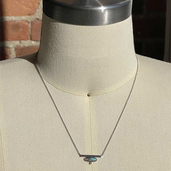 Front view of oval cut turquoise and round cut diamond bar necklace cast in 14 kt white gold on body form.